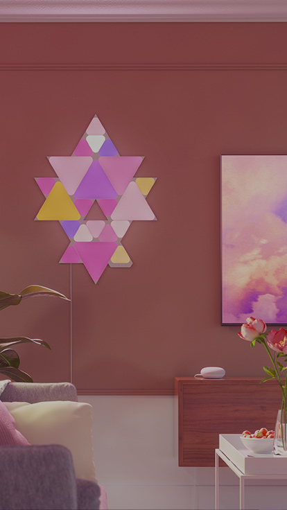 L’image représente une mise en forme réalisée à l’aide de Triangles et Mini Triangles Nanoleaf Shapes accrochés au mur à côté d’un téléviseur dans le salon. Les panneaux lumineux RVB sont reliés les uns aux autres à l’aide de connecteurs pour créer un motif.