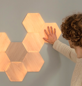 Questa è un'immagine di Nanoleaf Elements Wood Look Hexagons montato su parete. I pannelli luminosi smart reagiscono al tatto e alla musica e riempiono la tua casa di illuminazioni soffuse. Tocca questi pannelli effetto legno e riproduci le tue canzoni preferite per creare effetti luminosi dinamici.