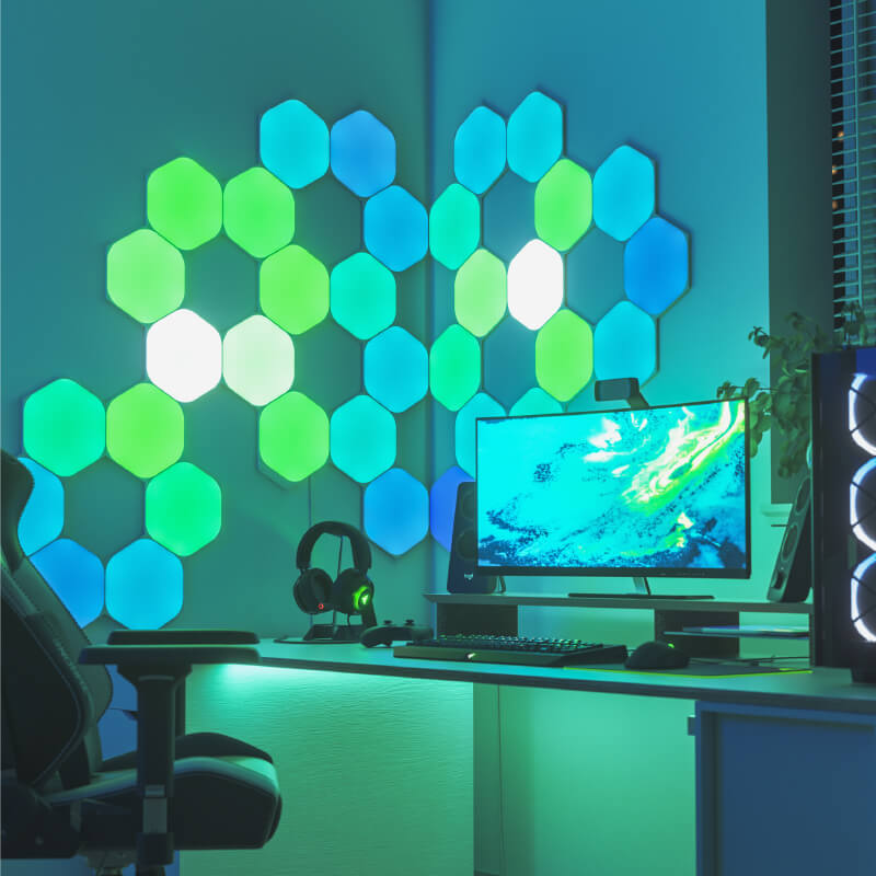 Panneaux lumineux modulaires intelligents hexagonaux à couleurs changeantes Nanoleaf Shapes compatibles Thread montés sur un mur au-dessus d’une battlestation. Semblables à Philips Hue, Lifx. HomeKit, Assistant Google, Amazon Alexa, IFTTT. 