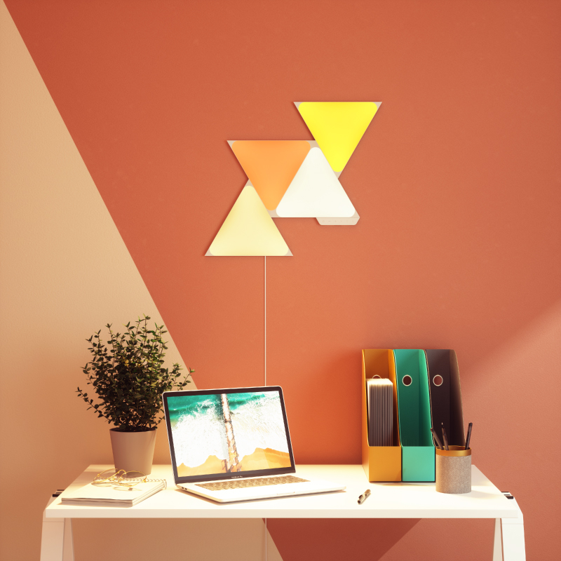 Nanoleaf Shapes Thread enabled color changing triangle smart modular light panels mounted to a wall above a desk. Similar to Philips Hue, Lifx. HomeKit, Google Assistant, Amazon Alexa, IFTTT.